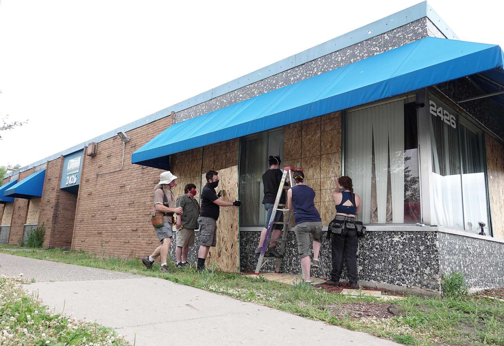 6 stagehands board up a business in the daylight